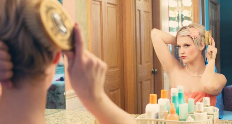 Woman brushing hair in mirror with bottles on sink