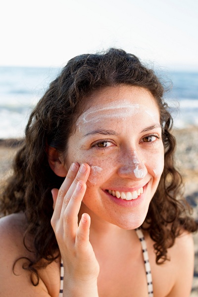 Happy woman applying sunscreen protection on face