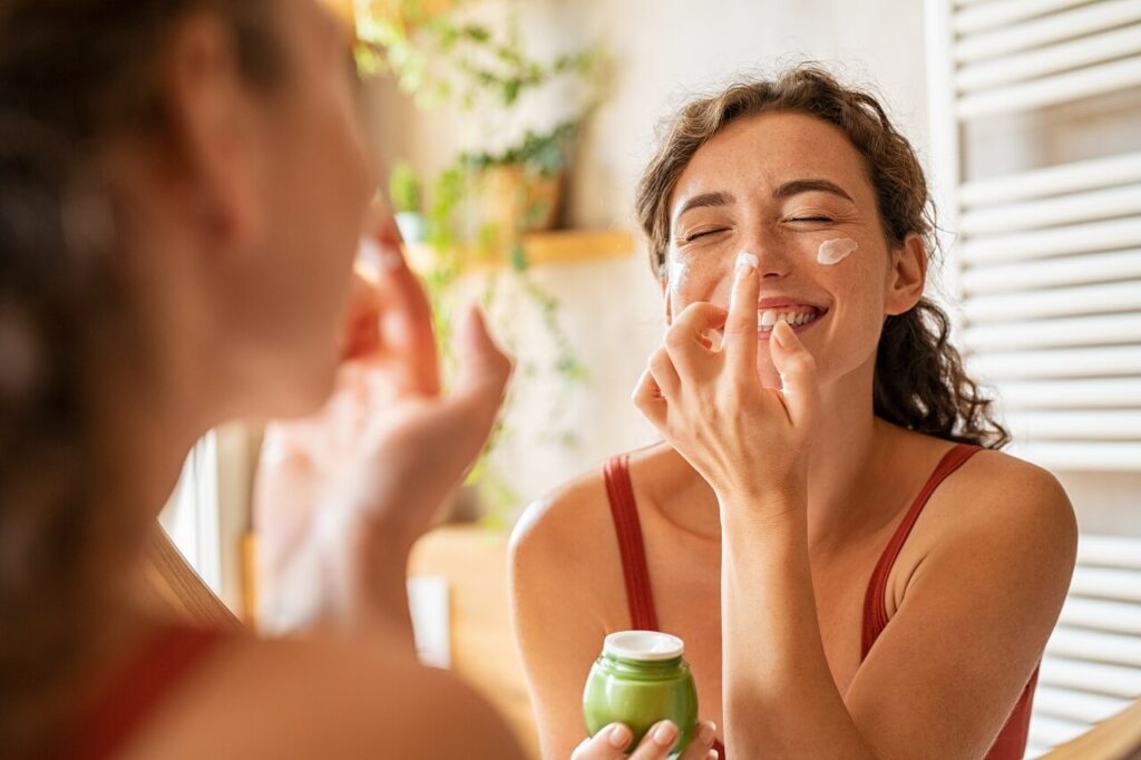 happy woman applying beauty cream on face