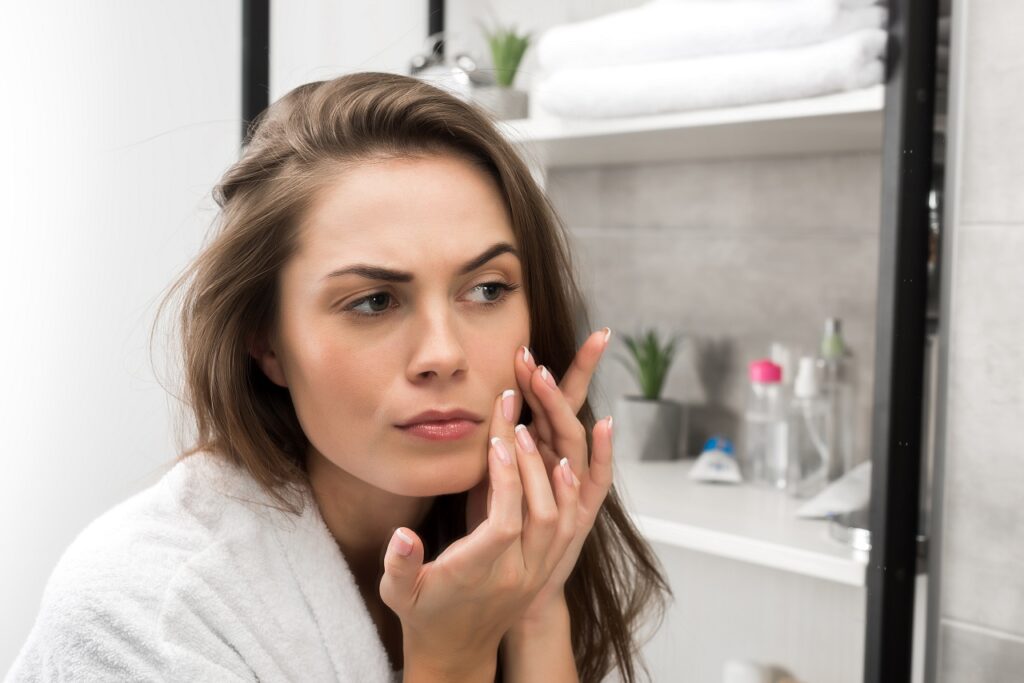 Woman checking face skin and looking at the mirror